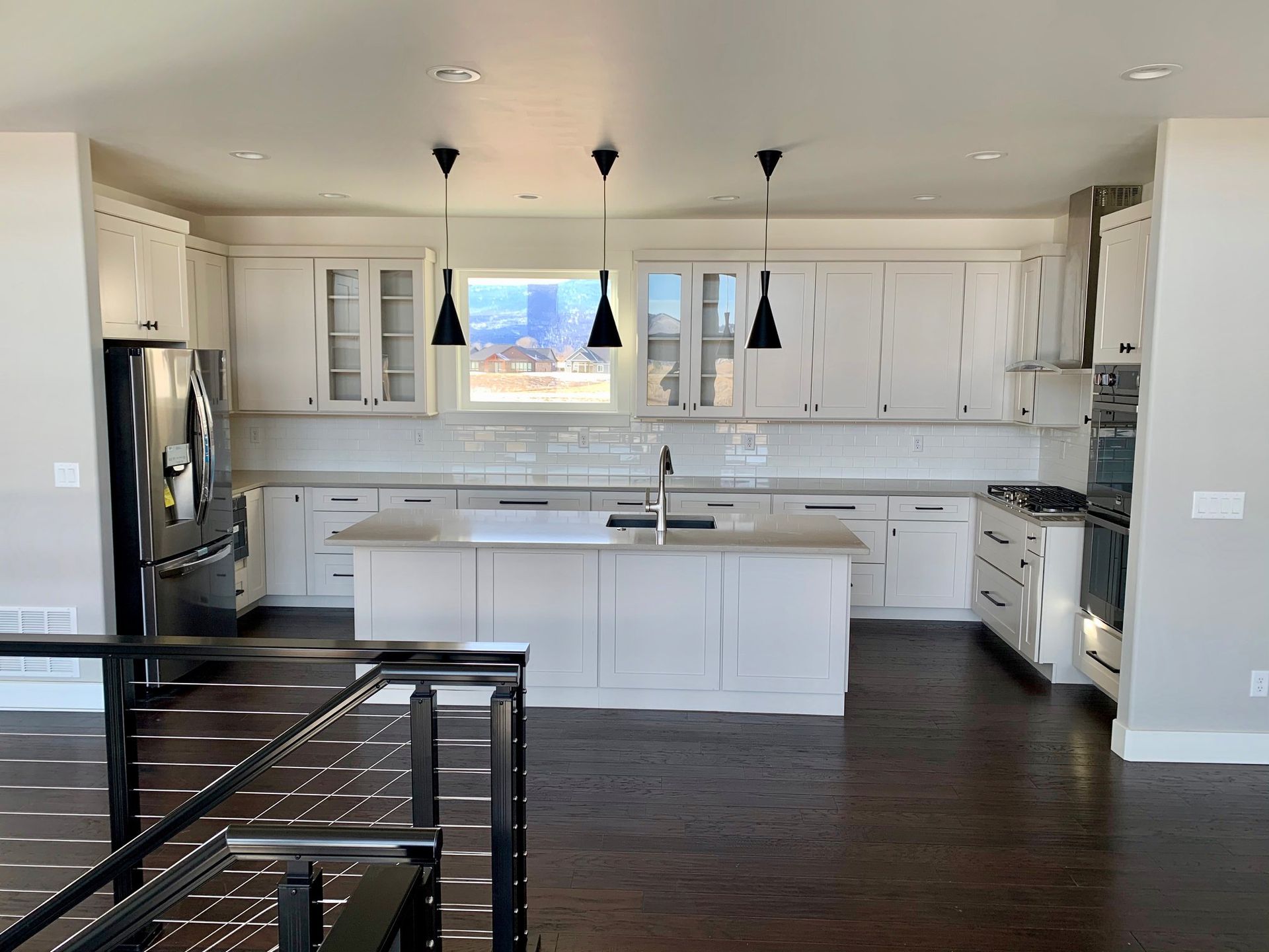 Modern kitchen with white cabinets, black island, stainless fridge, and pendant lights.