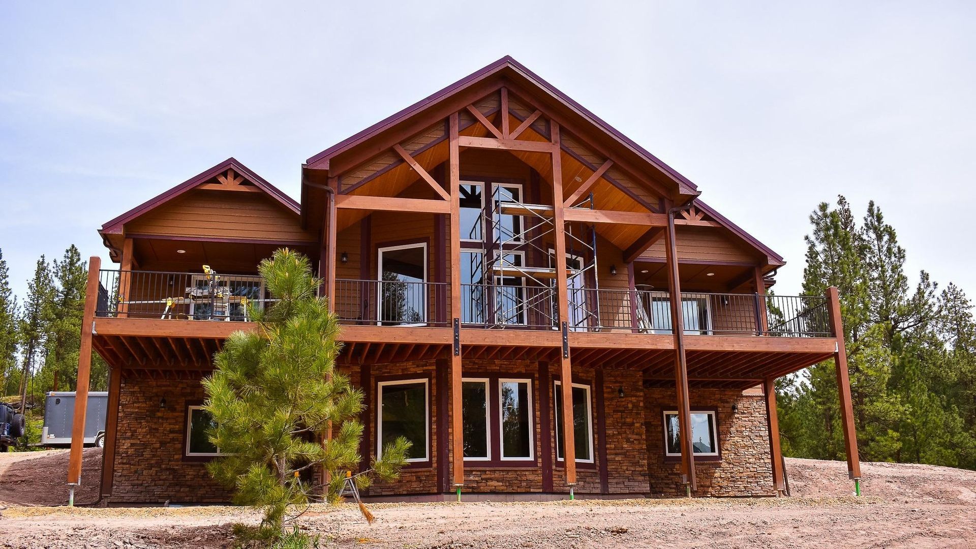 Large rustic wooden mountain lodge with balconies and tall windows, surrounded by trees under a clear sky