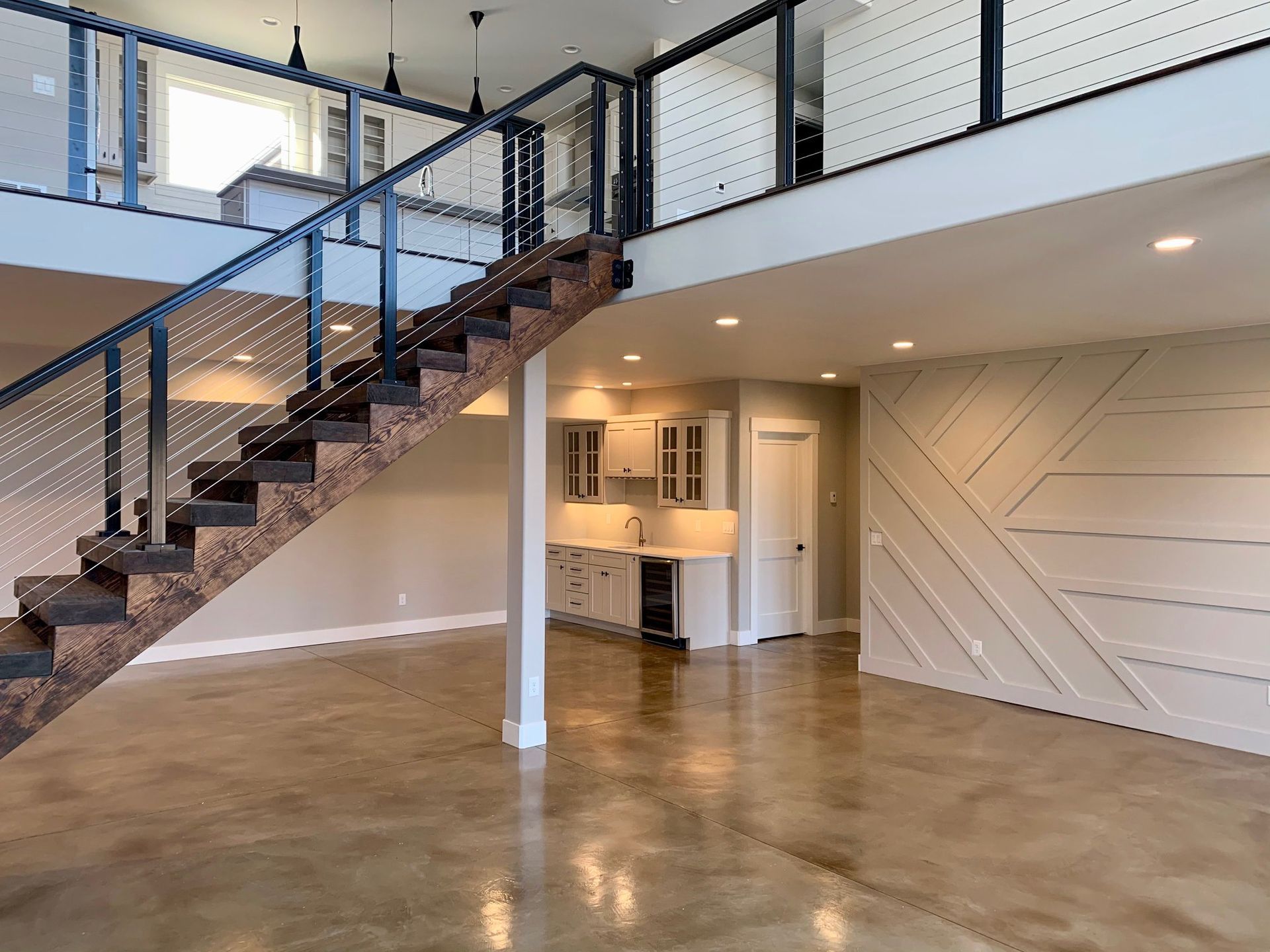 Loft-style interior with metal staircase, mezzanine railing, polished concrete floor, and kitchen nook