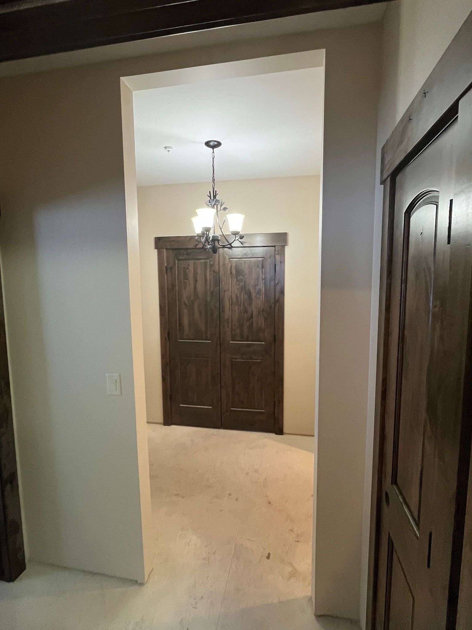 Hallway view into a carpeted room with dark wood double doors and a hanging chandelier.