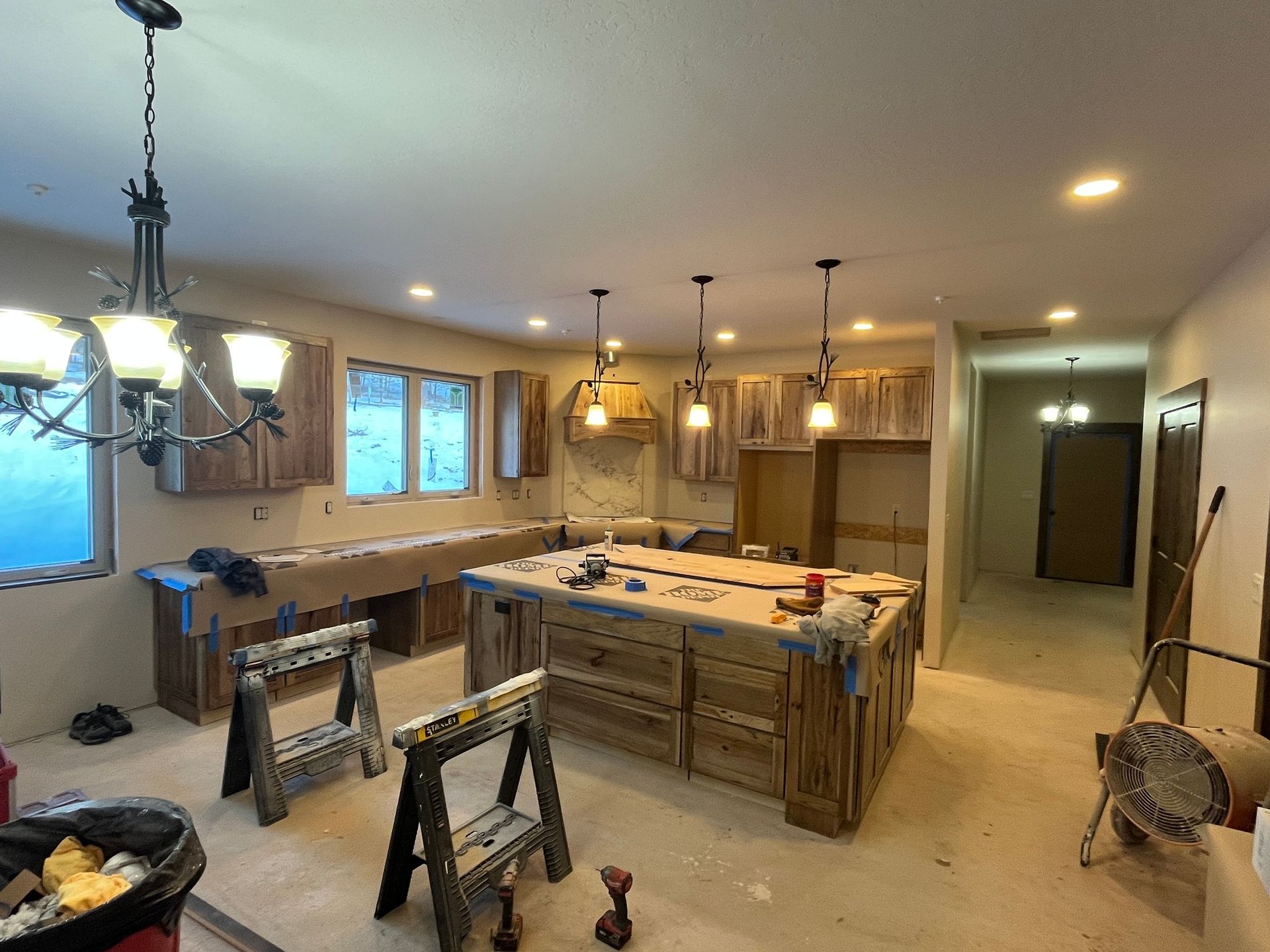 Unfinished kitchen with island, pendant lights, ladder, and tools in a renovated open-plan room