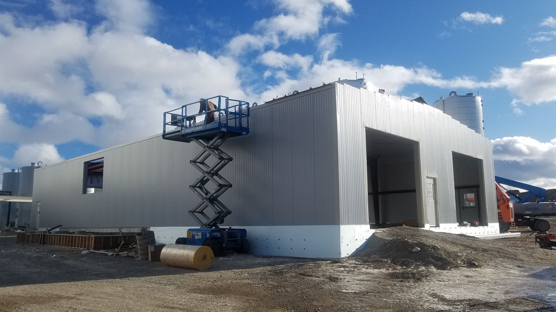 Construction trailer with white siding and blue lift under a partly cloudy sky