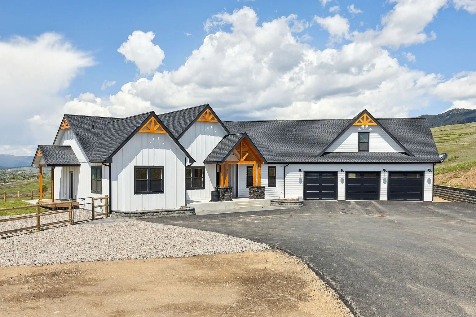 Modern white house with gray roof, black garage doors, and a gravel driveway under a cloudy sky