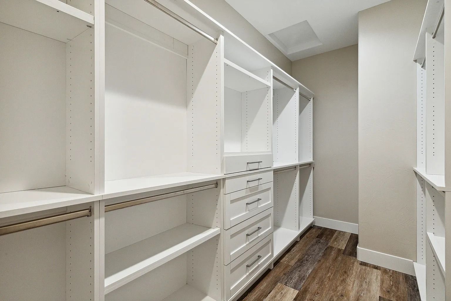 White walk-in closet with shelving, drawers, and hanging rods on wood flooring
