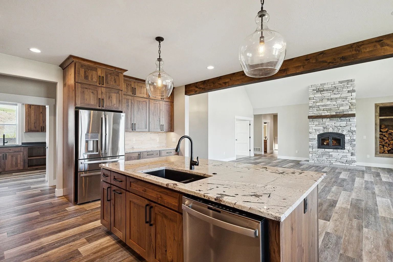 Modern kitchen with granite island, stainless appliances, and open view to a stone fireplace living room
