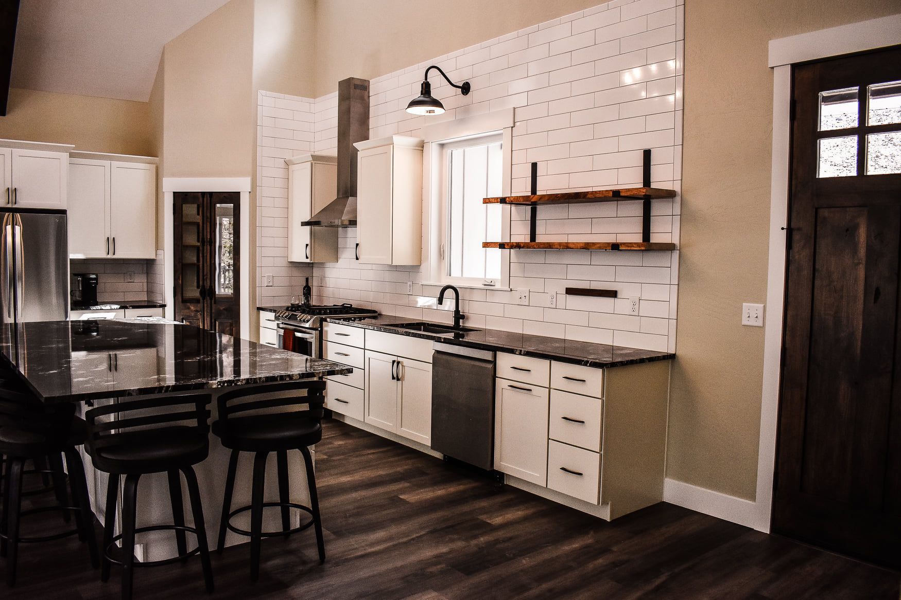 Modern kitchen with white cabinets, black countertops, island seating, and dark wood floors