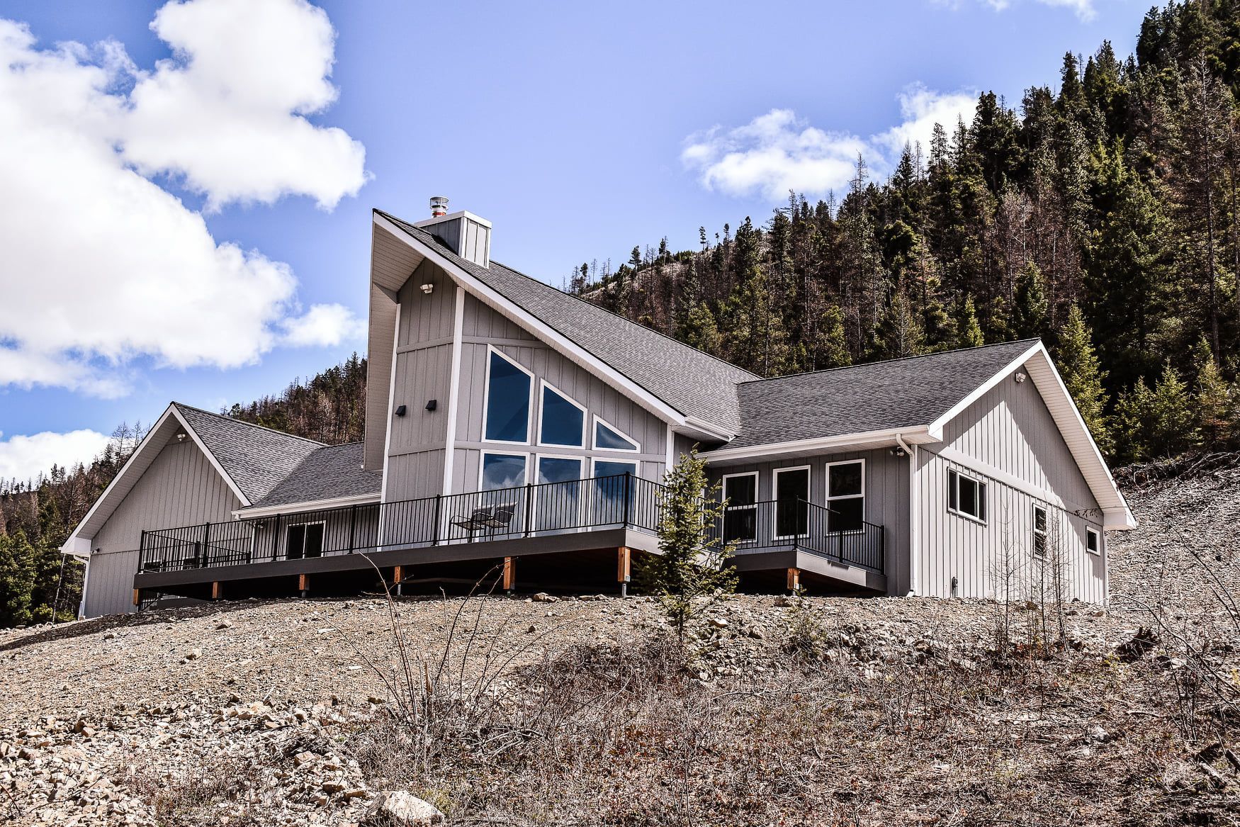 Modern white A-frame house with large windows on a rocky hillside under a blue sky