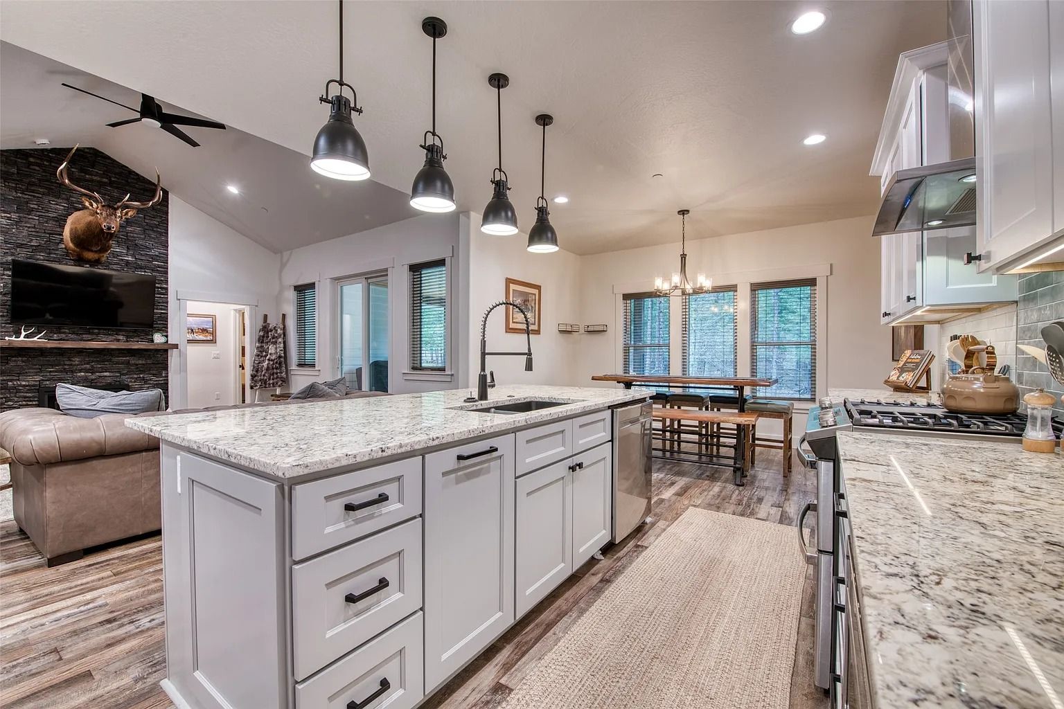 Bright modern kitchen with white cabinets, granite island, pendant lights, and dining area beyond