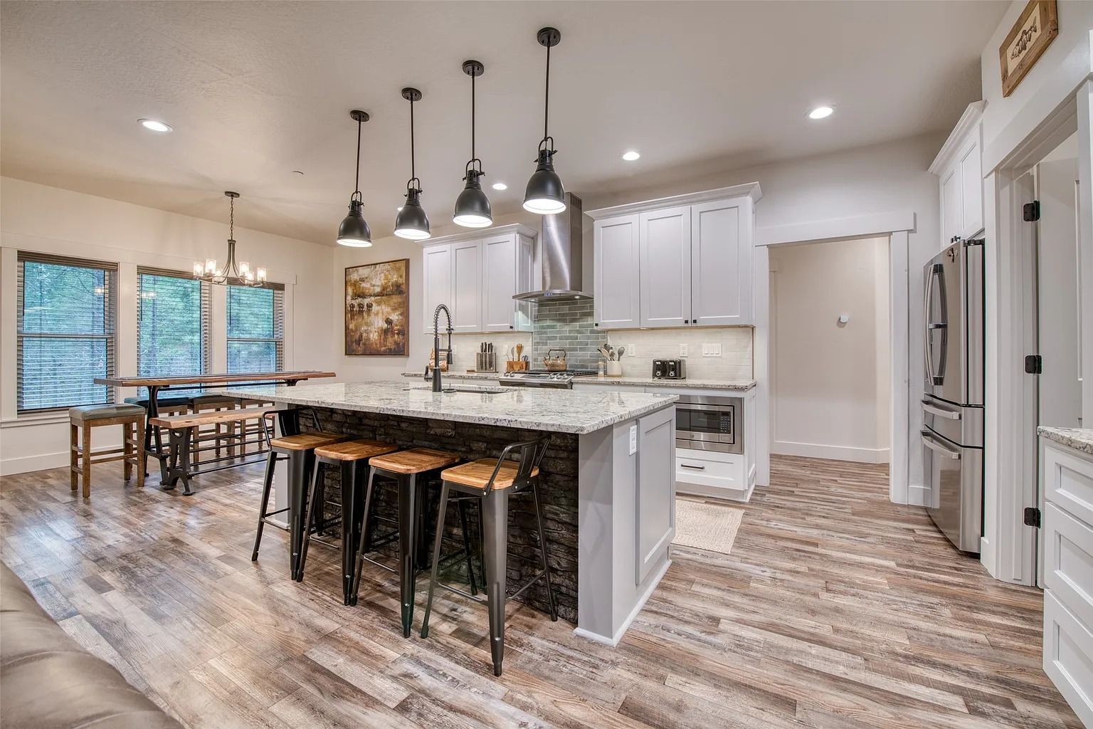 Modern kitchen with granite island, black bar stools, pendant lights, and open dining area.