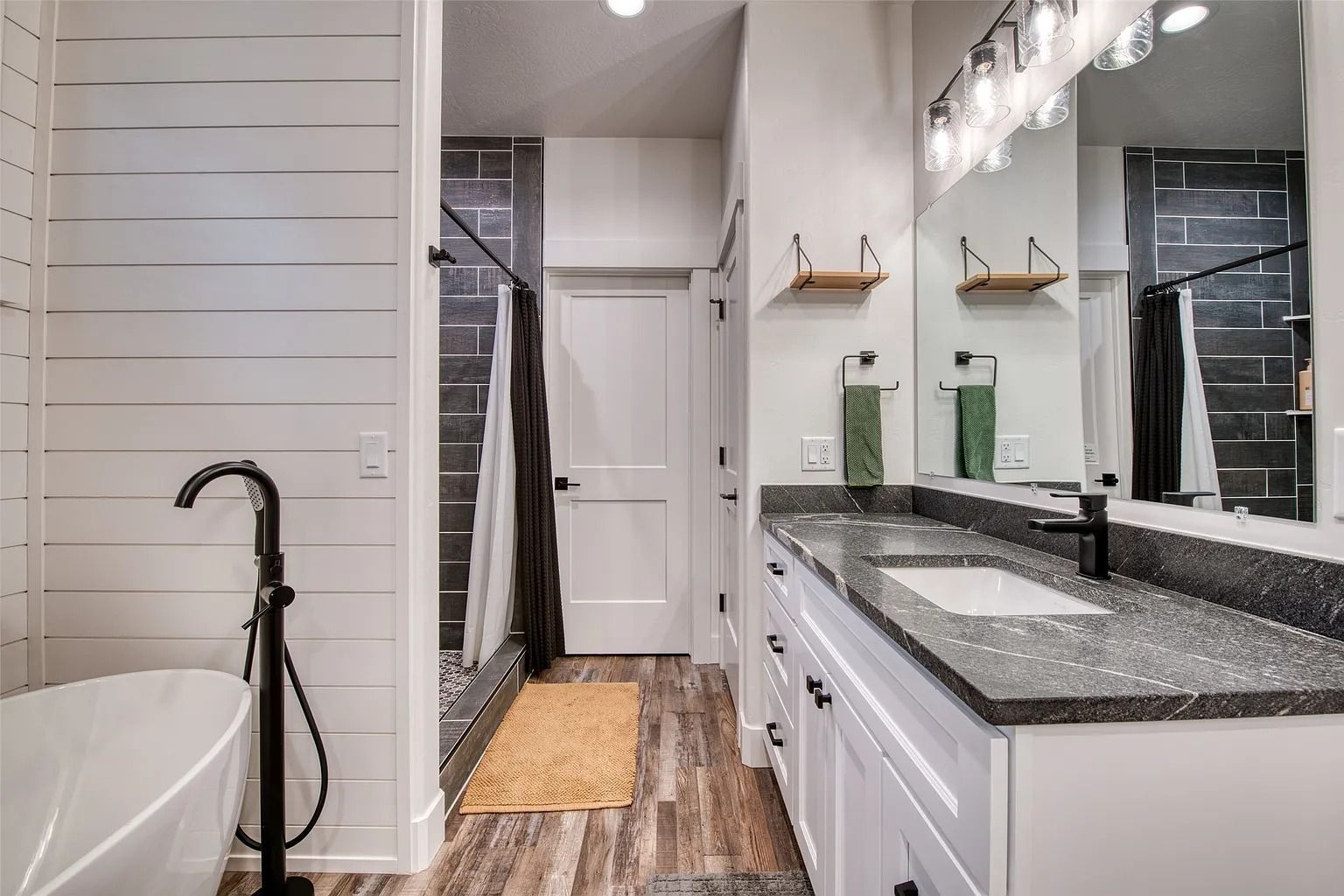 Modern bathroom with a long vanity, large mirror, black fixtures, and freestanding tub