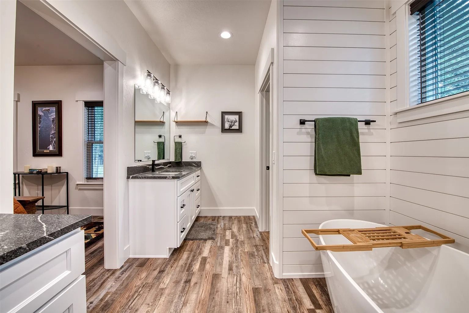 Bright bathroom with white shiplap walls, wood-look floor, and freestanding tub with green towel.