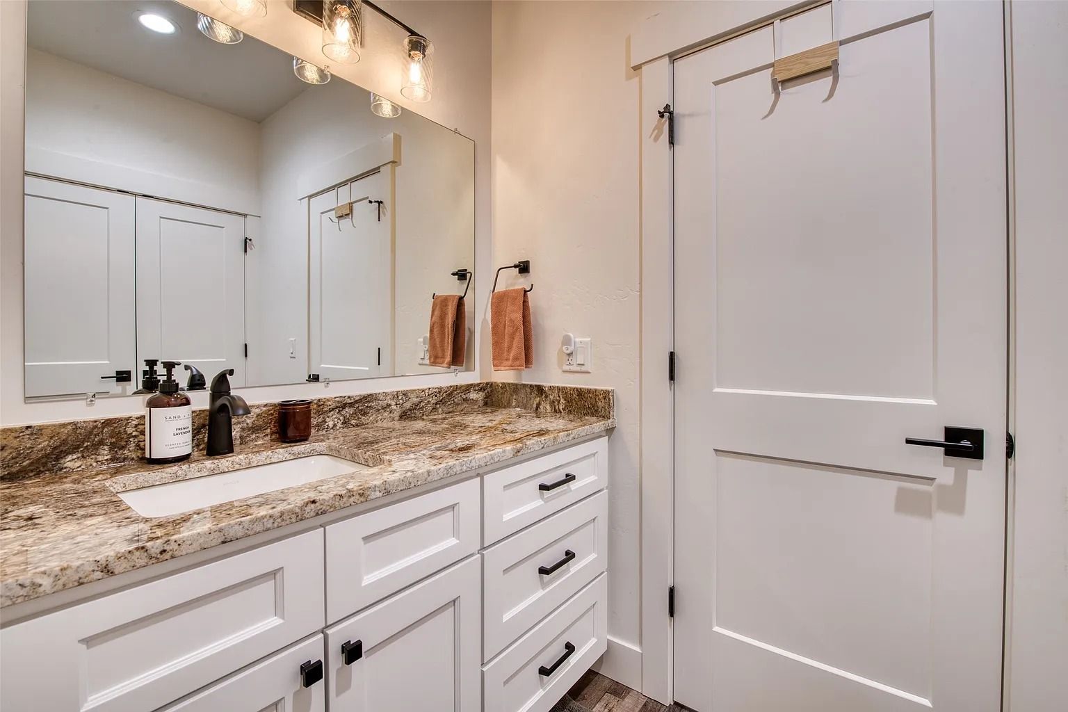 Bright bathroom vanity with granite countertop, double mirror, white cabinets, and a closed door.