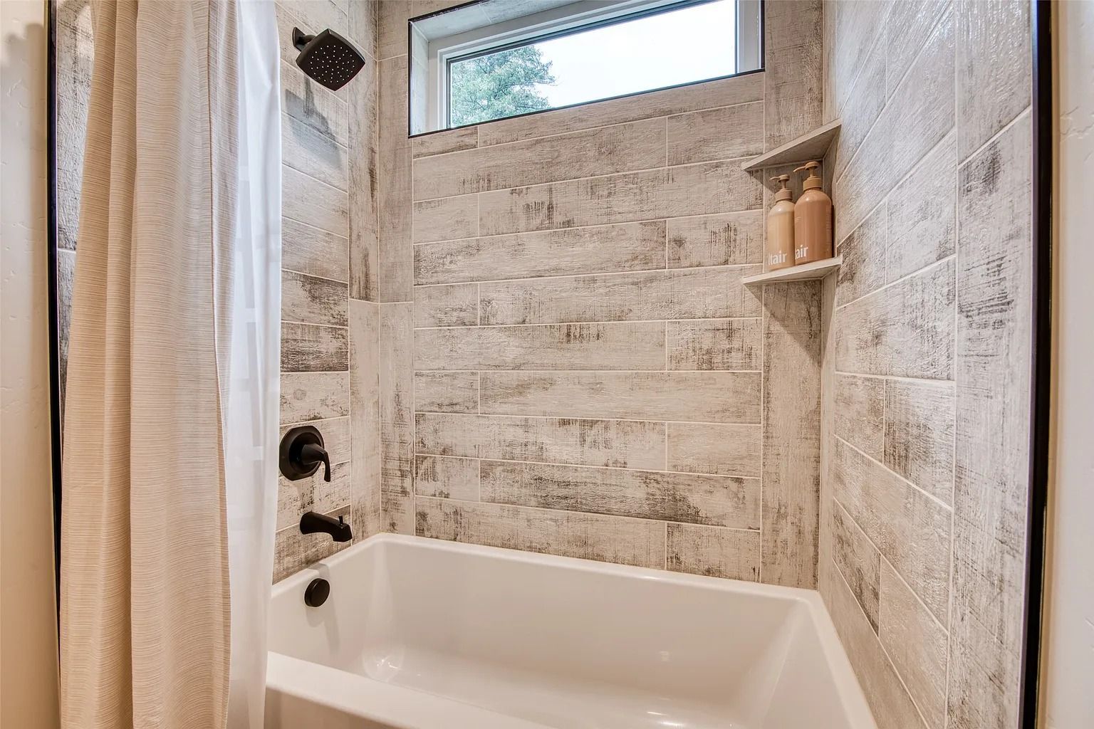 Modern bathroom shower-tub combo with textured tile walls and a small high window