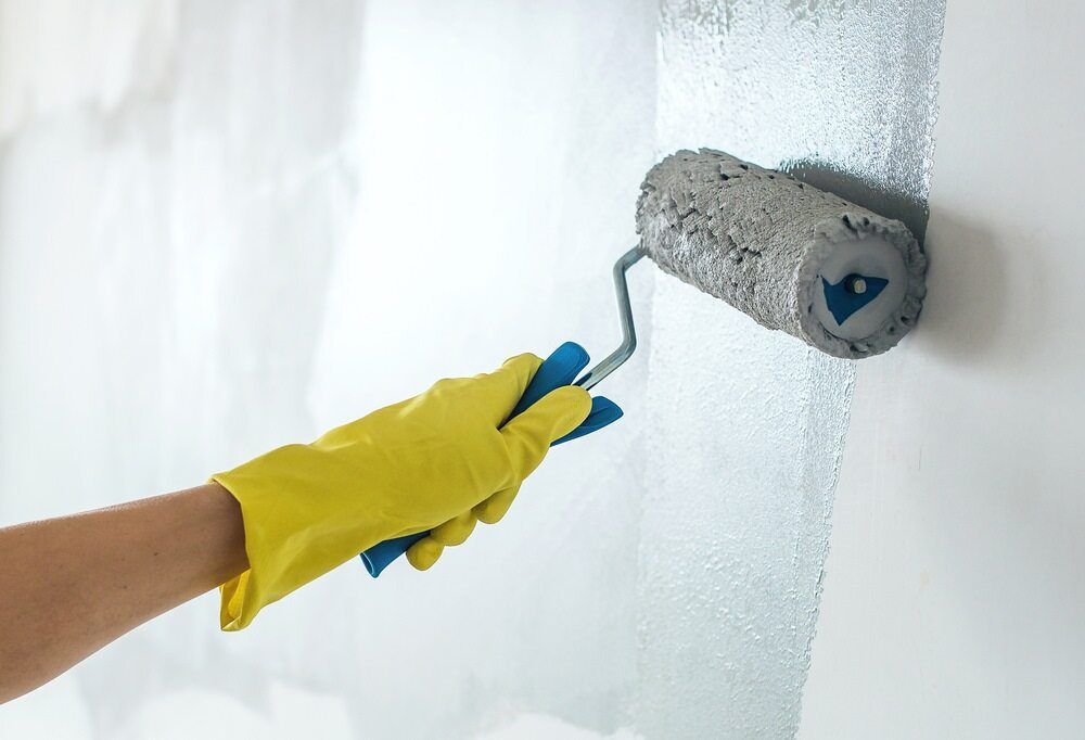 A Person Wearing a Yellow Glove is Painting a Wall With a Paint Roller — Prota NT in Howard Springs, NT