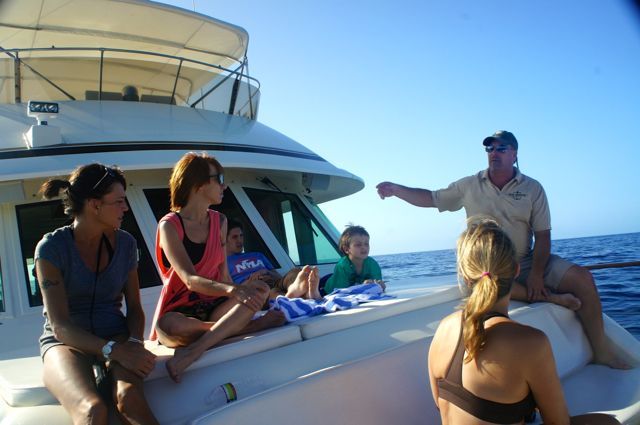 A group of people sitting on a boat with a man pointing
