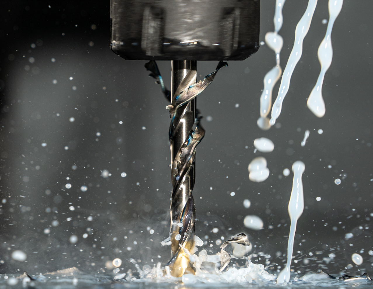 CNC milling machine cutting into a metal block, generating wood shavings in a workshop.