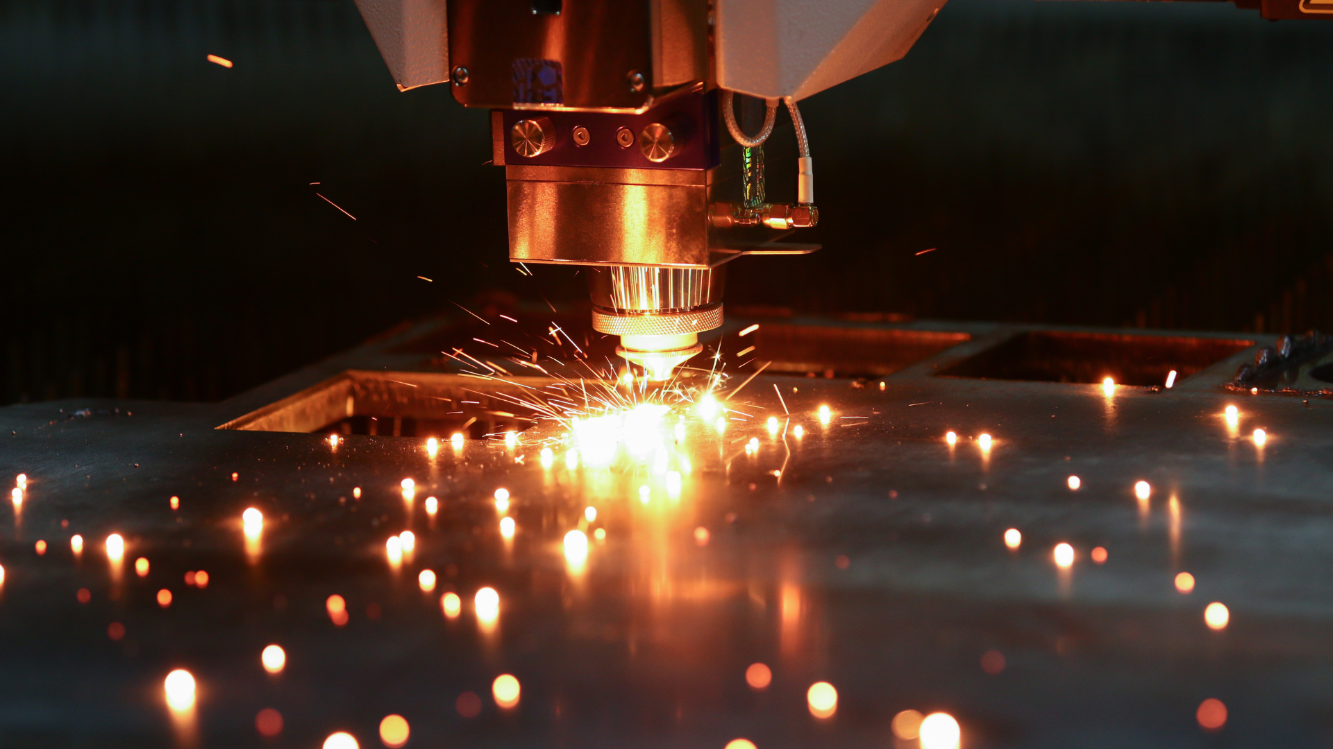 Laser cutting metal sheet, generating sparks and bright light.