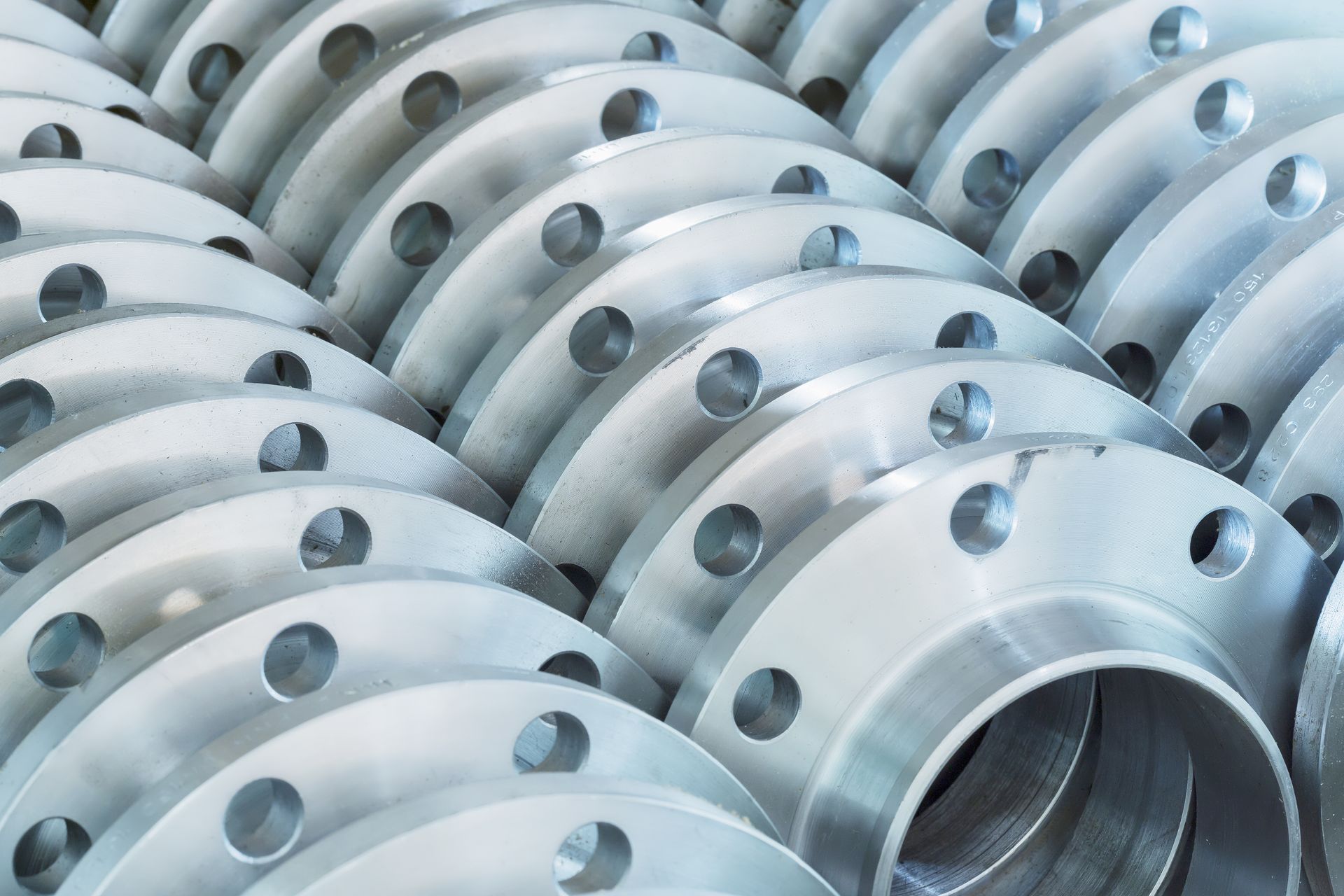Close-up of a stack of silver metal pipe flanges with bolt holes, ready for industrial use.