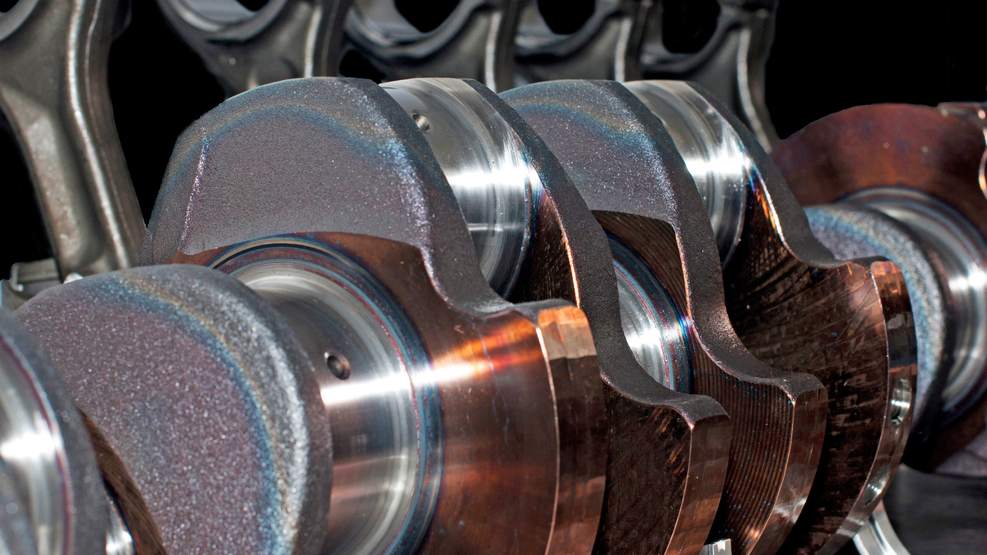Close-up of an engine crankshaft, showing rotating parts with a brown-bronze hue.