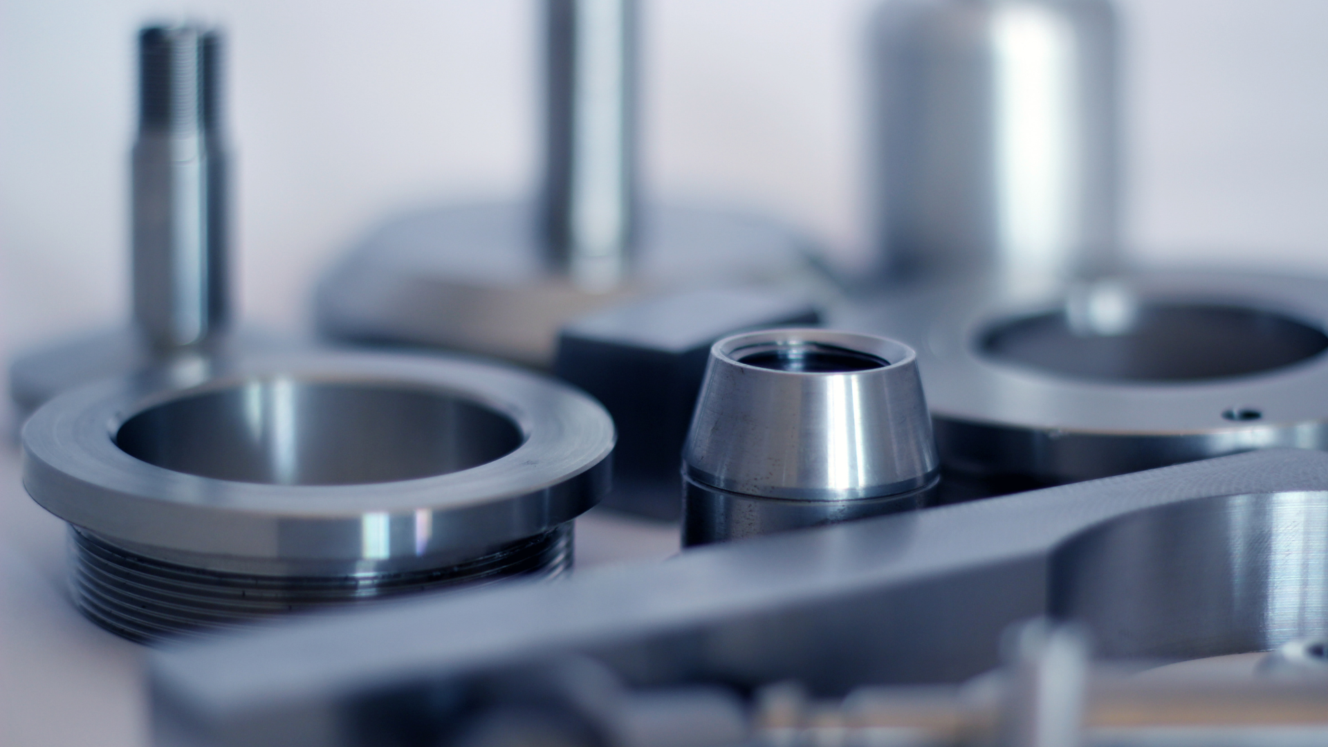 Close-up of various machined metal parts with a shiny, silver finish, against a light background.