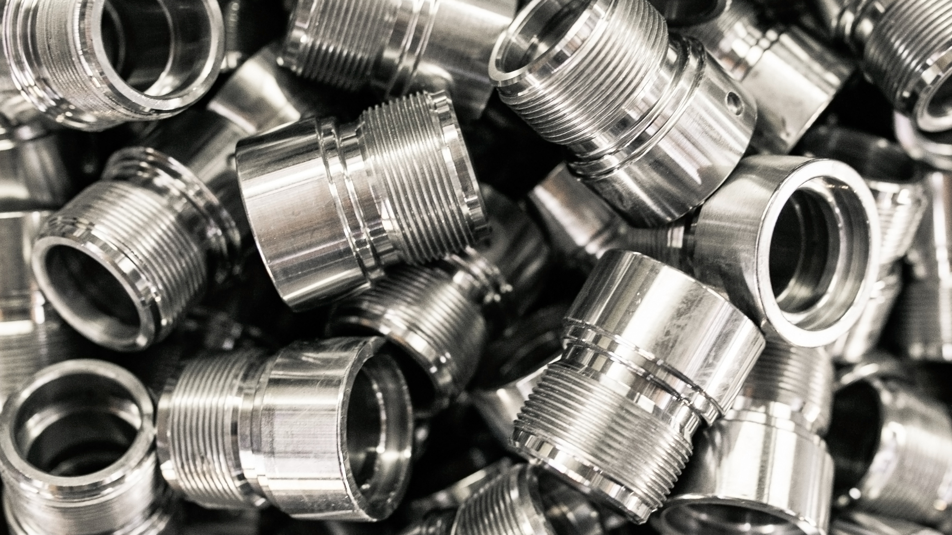 Pile of shiny, metal threaded components, possibly for machinery or industrial use.