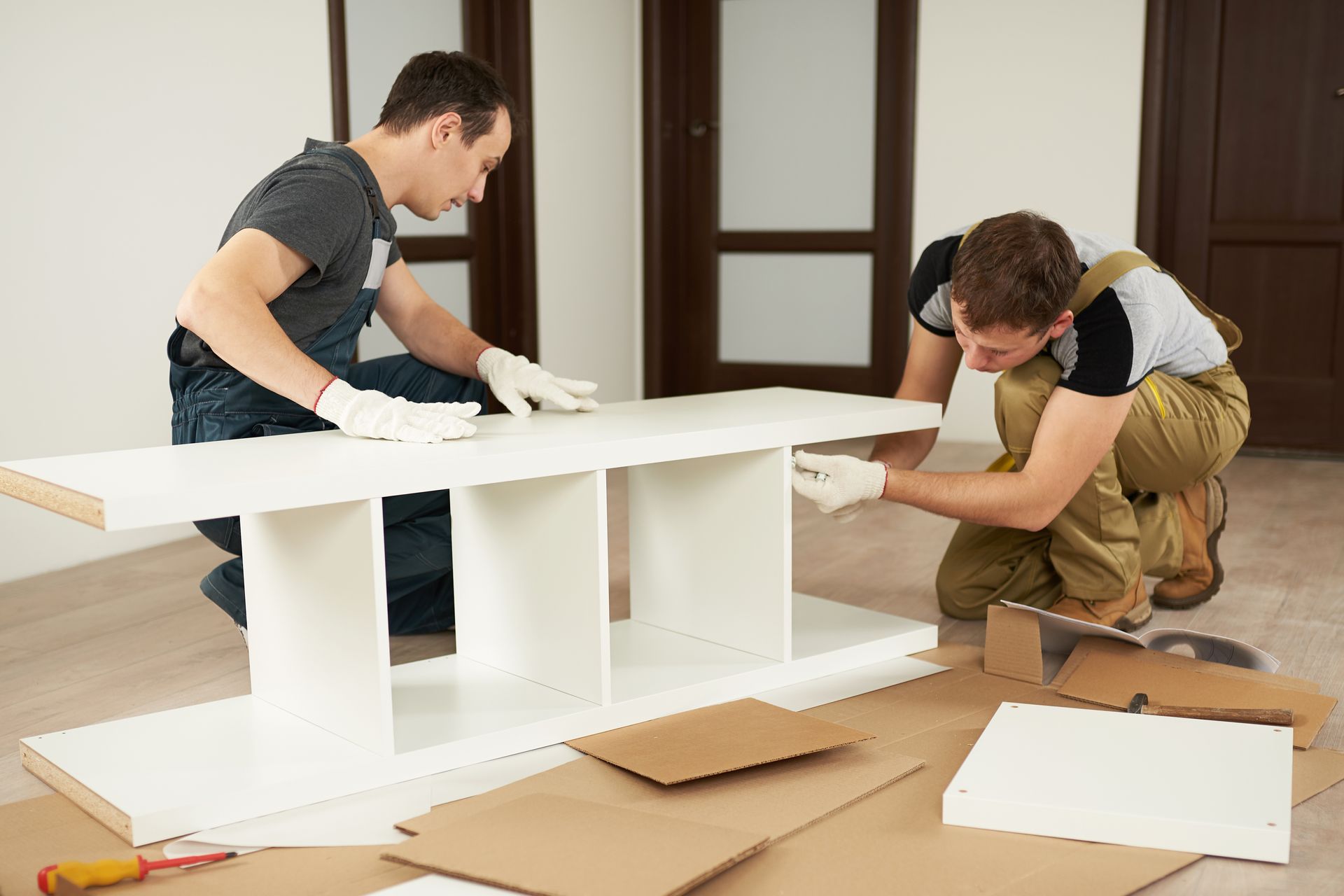 Two men are assembling a white shelf in a room.