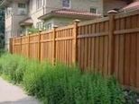 A wooden fence surrounds a lush green yard in front of a house.