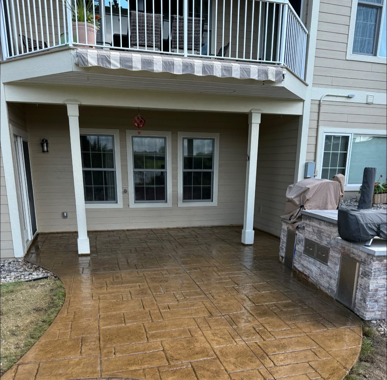 A patio with stamped concrete, under a balcony, and a grill.