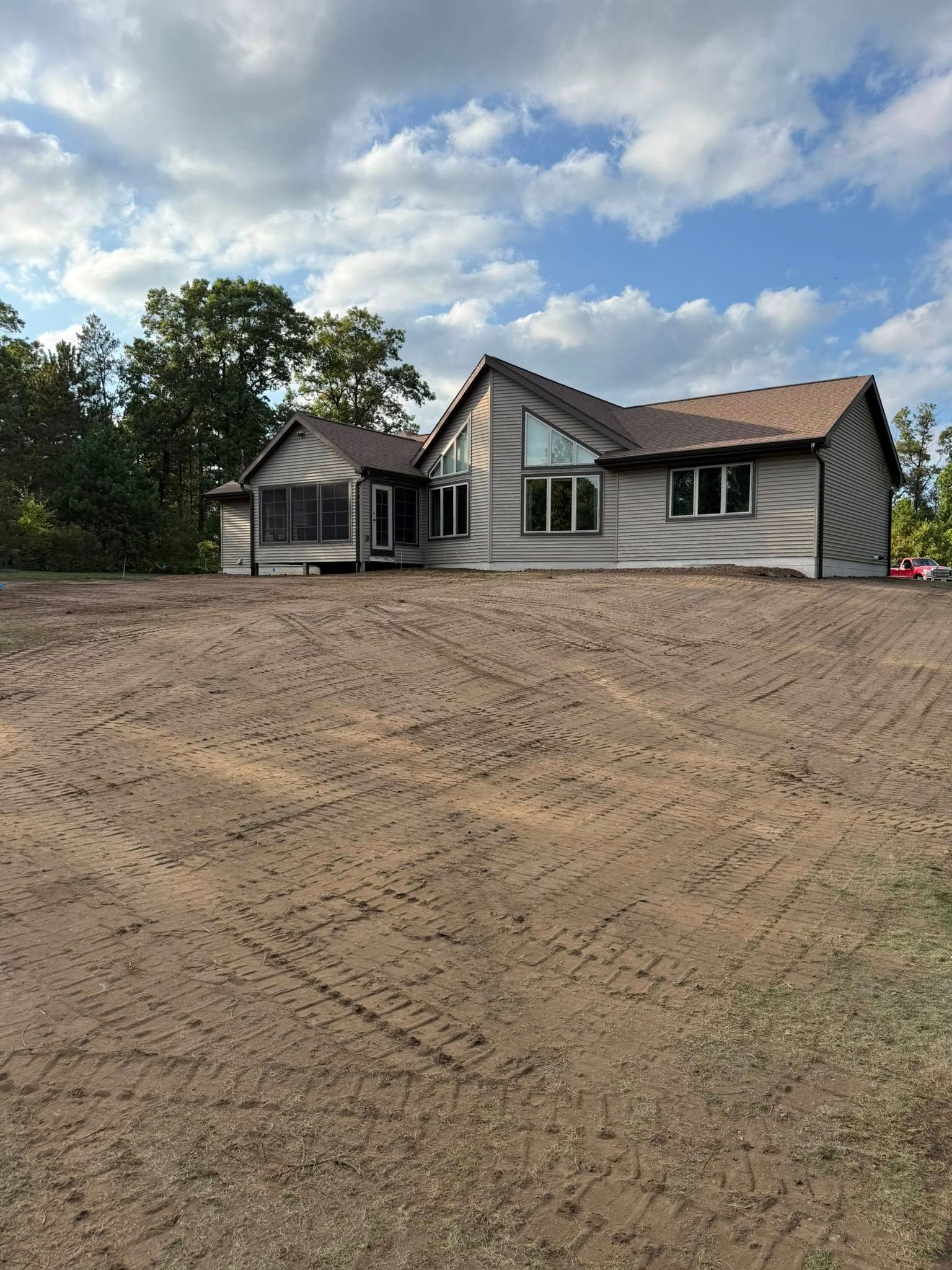 Gray house on a dirt lot under a partly cloudy blue sky.