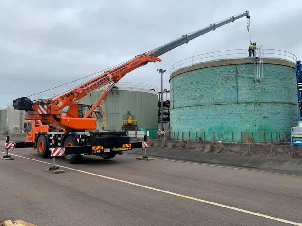 A Large Orange Crane Is Sitting In Front Of A Large Green Tank — Port Stephens Cranes In Salt Ash, NSW