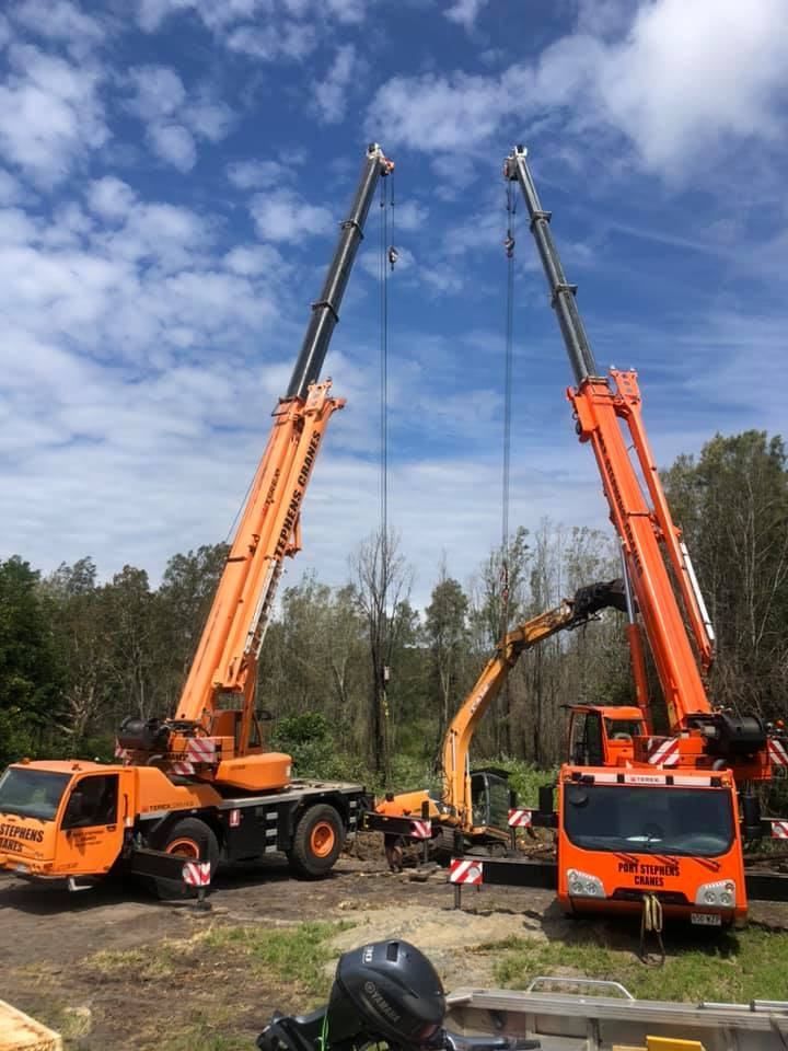 Two Orange Crane Trucks Are Parked Next To Each Other In A Field — Port Stephens Cranes In Salt Ash, NSW