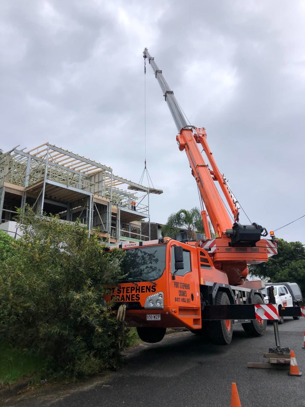 A Large Orange Crane Is Parked In Front Of A Building Under Construction — Port Stephens Cranes In Salt Ash, NSW