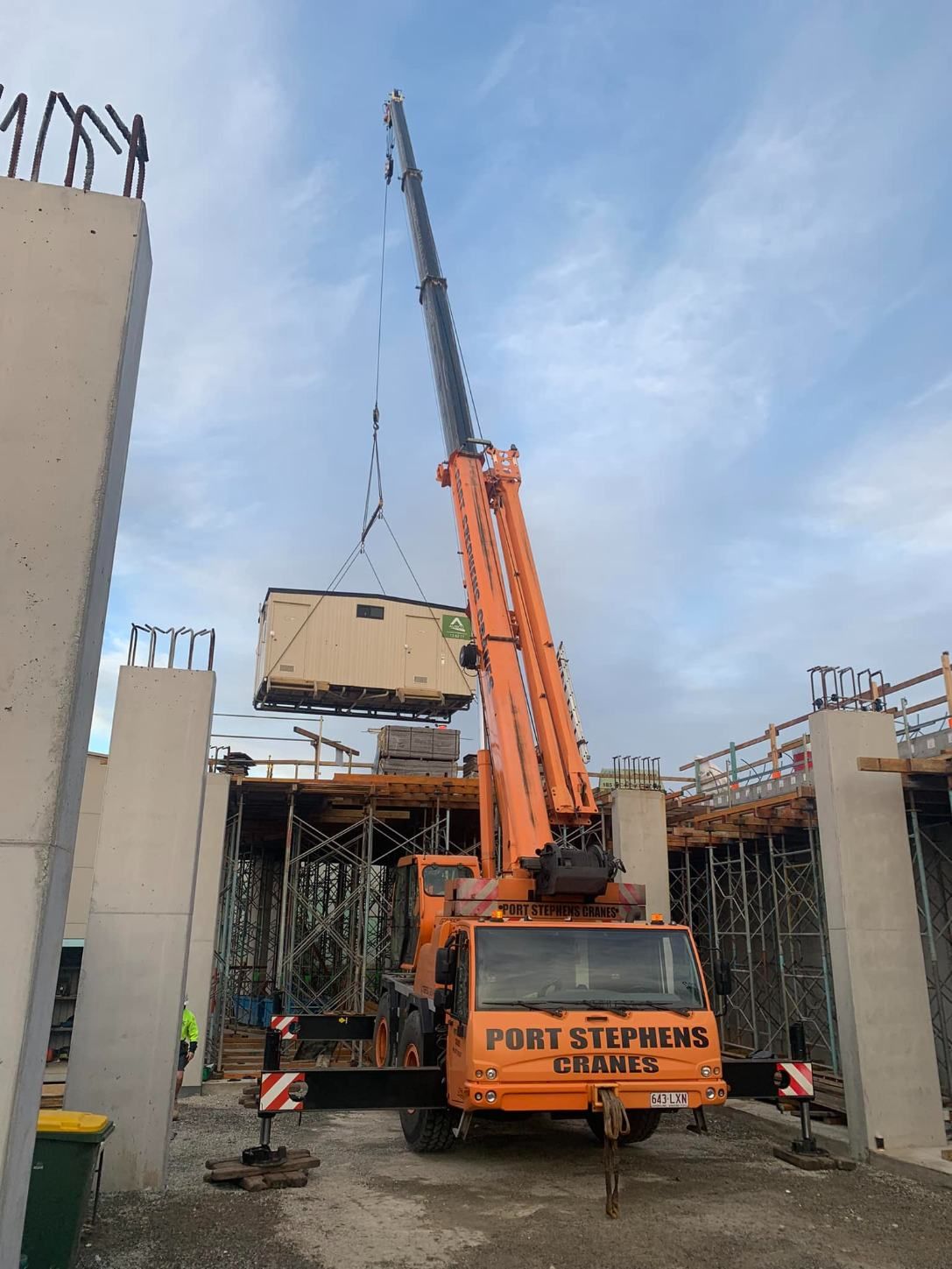 A Large Orange Crane Is Lifting A Small Building In A Construction Site — Port Stephens Cranes In Port Stephens, NSW