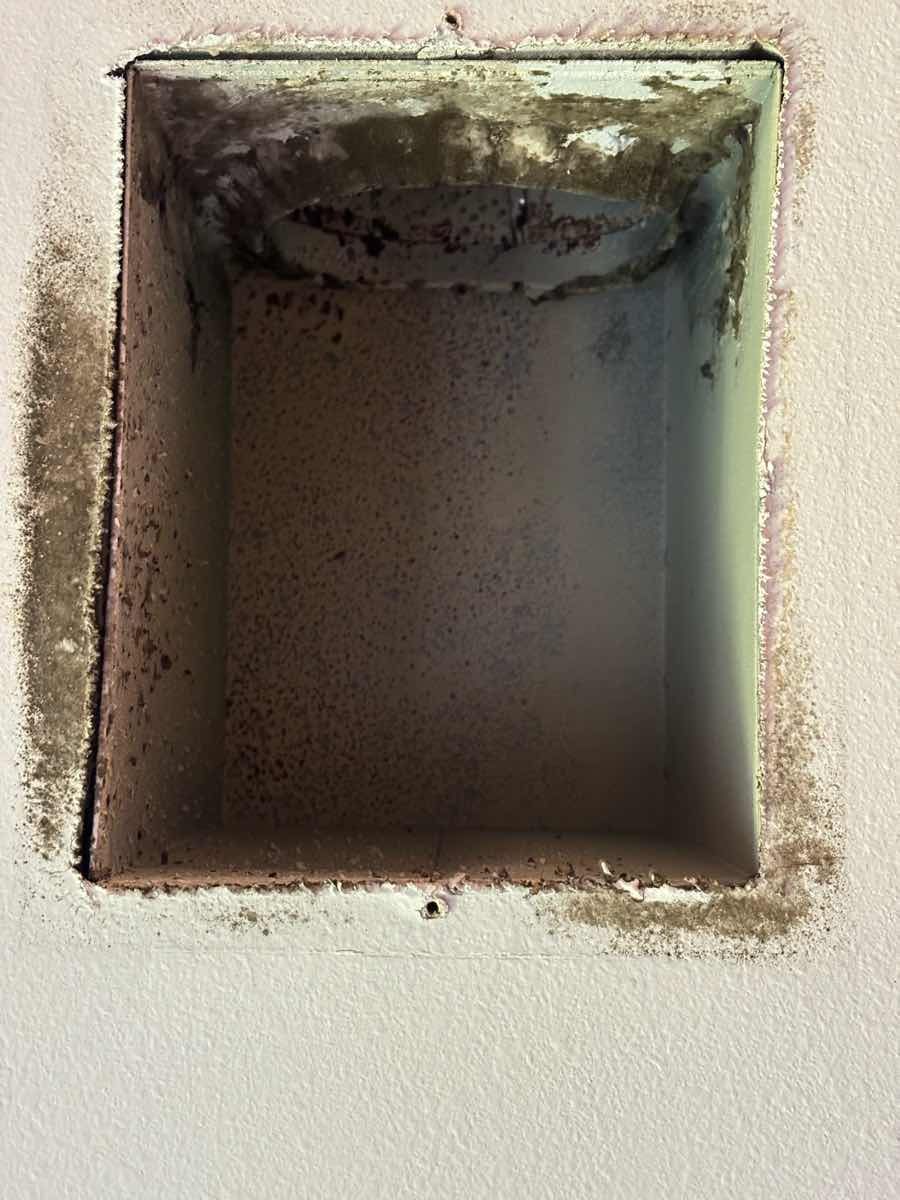 Inside a dirty air duct, dust and debris cover the bottom. Two gray, cylindrical supports are visible.