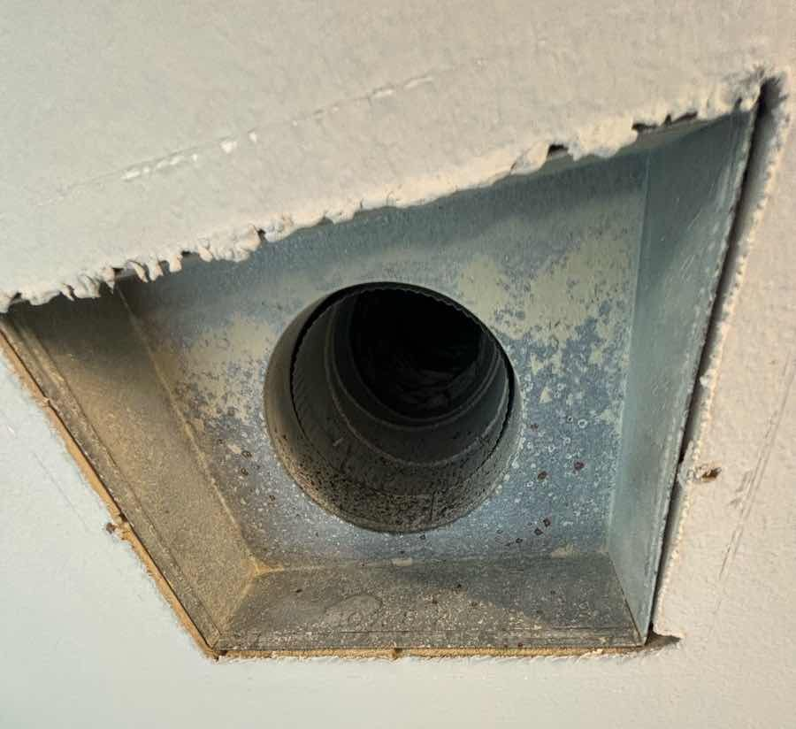 Inside view of a rectangular duct, light brown insulation, with a silver metal support in the center. Dark tunnel ahead.