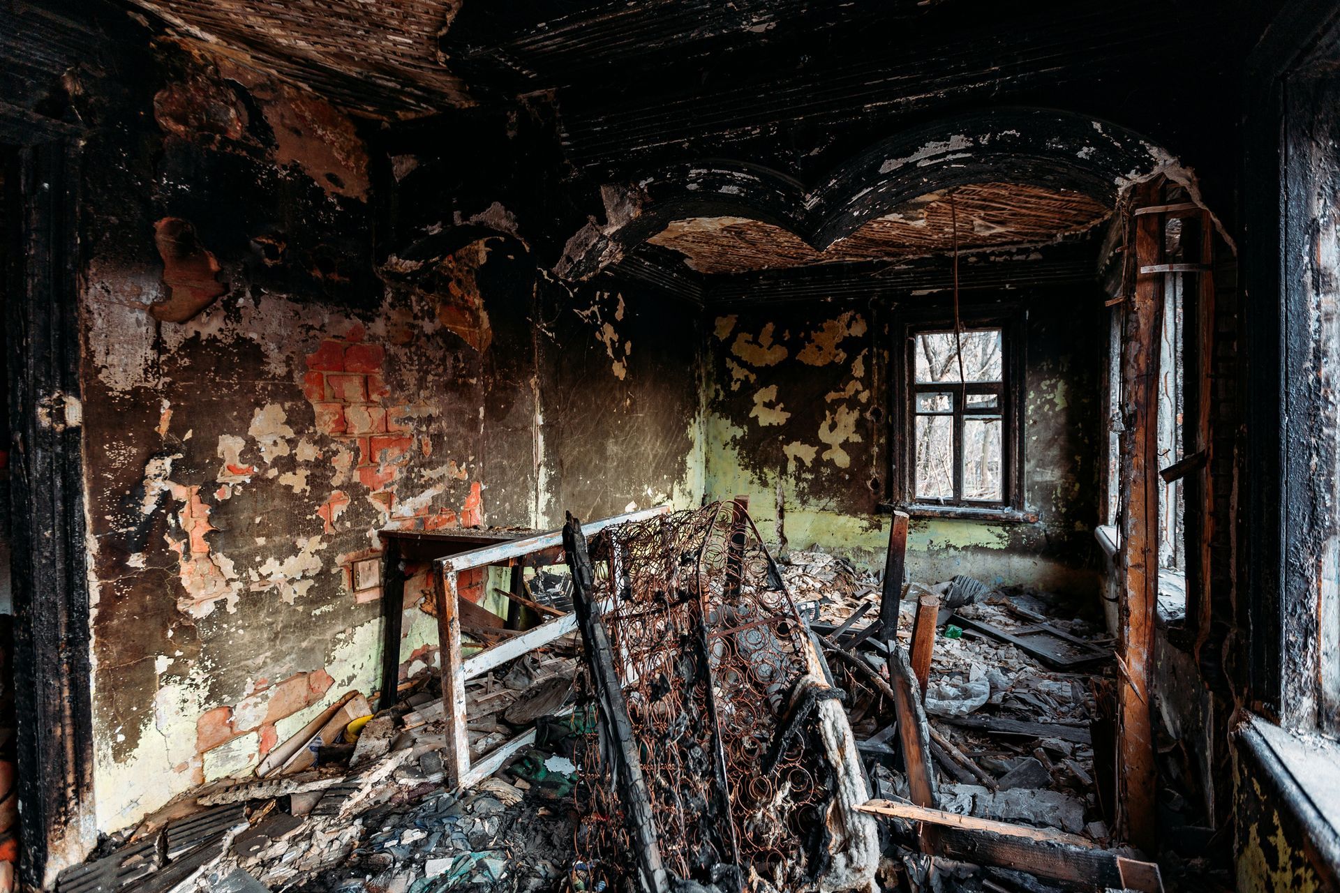 Interior of a burned room, debris-filled, with charred walls and a window.
