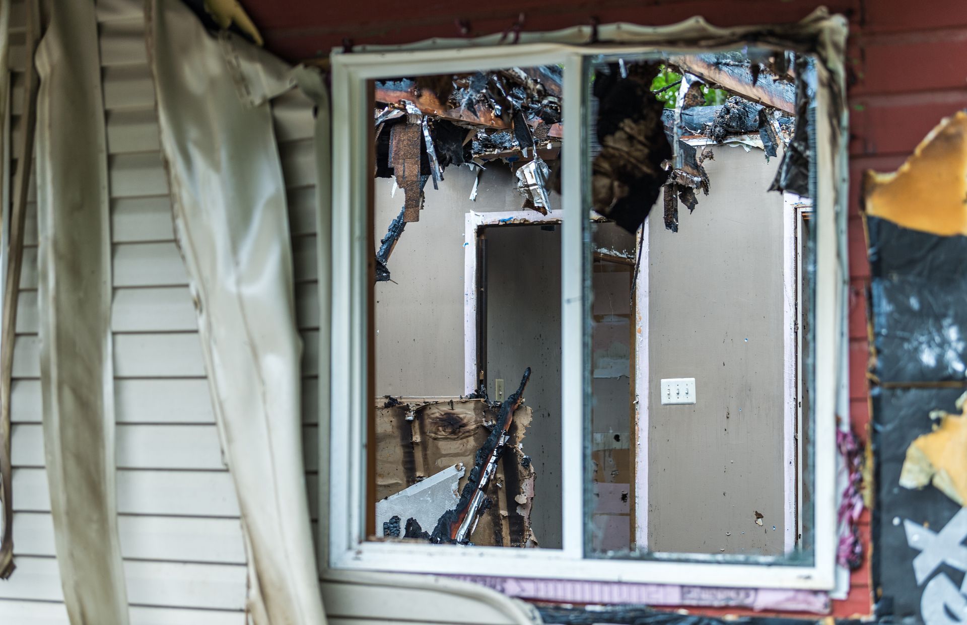 A home destroyed by a fire with melted vinyl siding, roof collapse, and burned furniture.