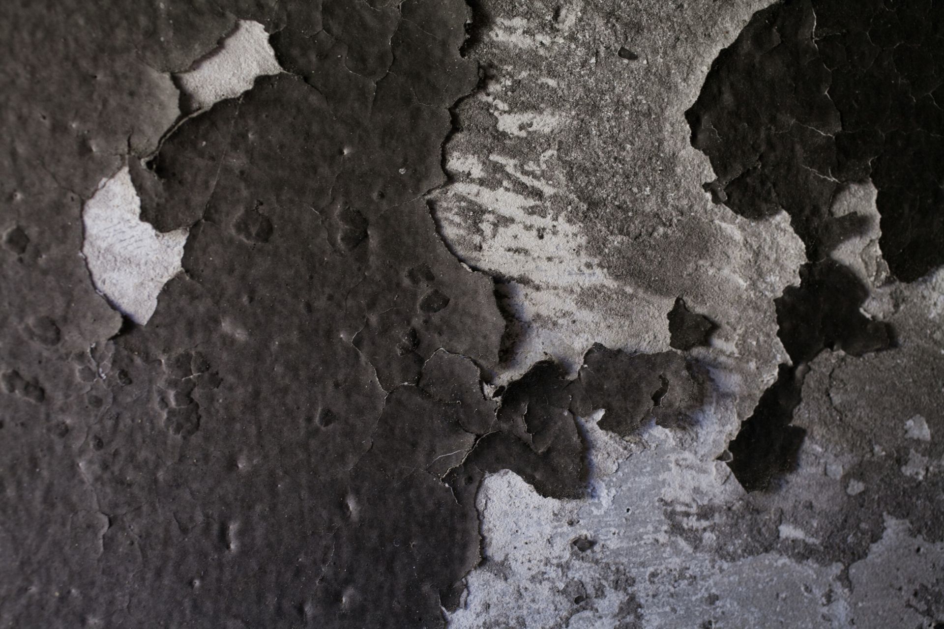 Cracked, peeling black paint on a gray wall, revealing the surface beneath.