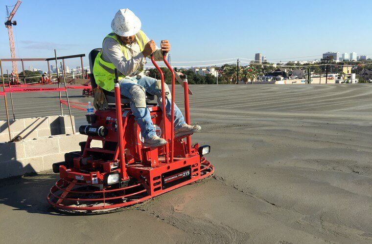 A construction worker is riding a machine on a concrete surface.