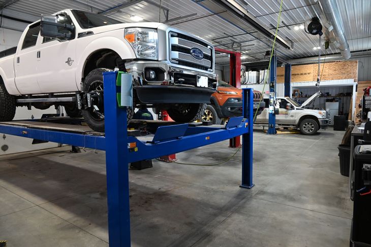 Lifted, mint green and dark green Ford pickup truck with chrome roll bar and oversized tires.