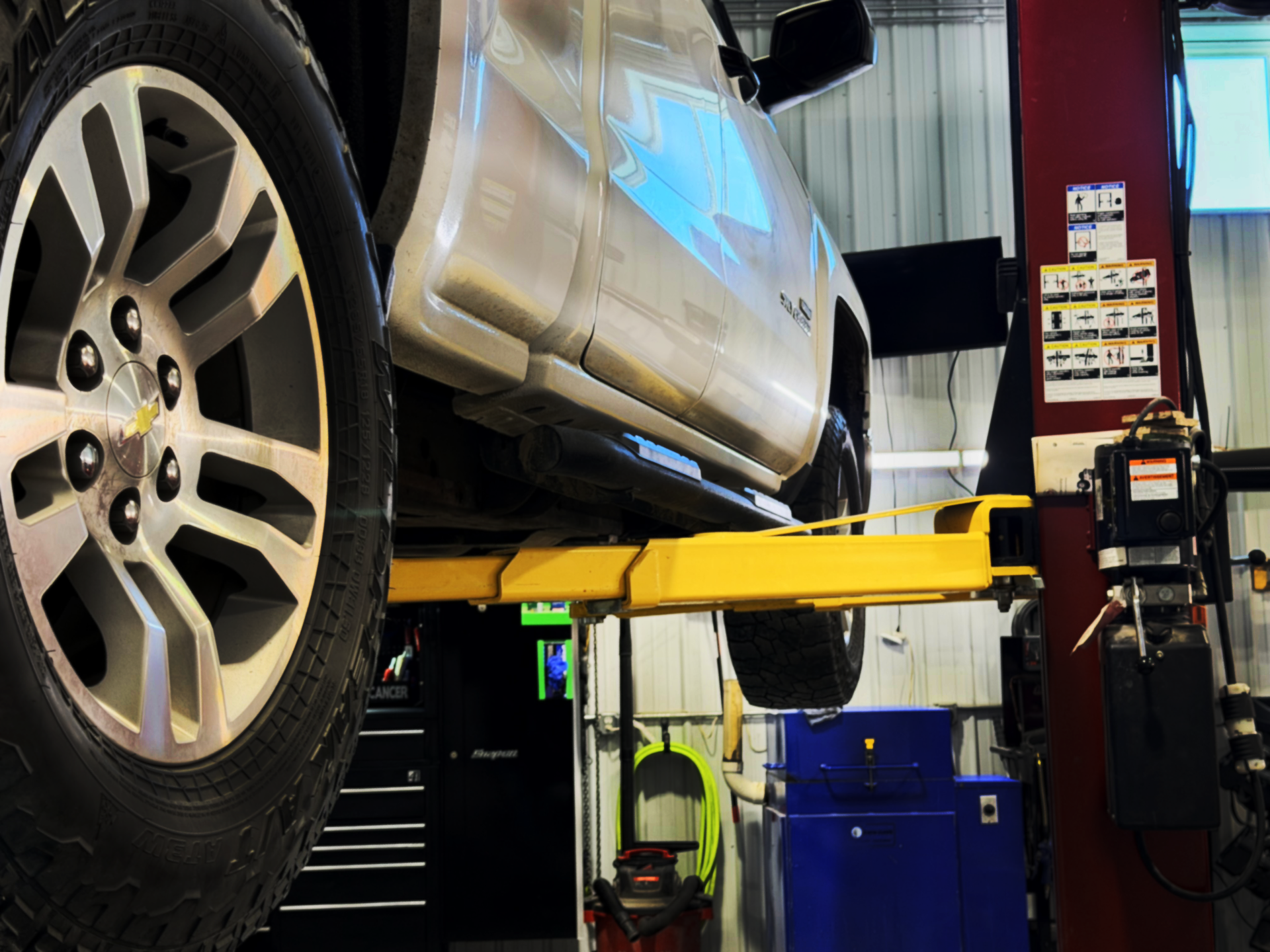 Silver truck on a yellow lift in an auto repair shop.