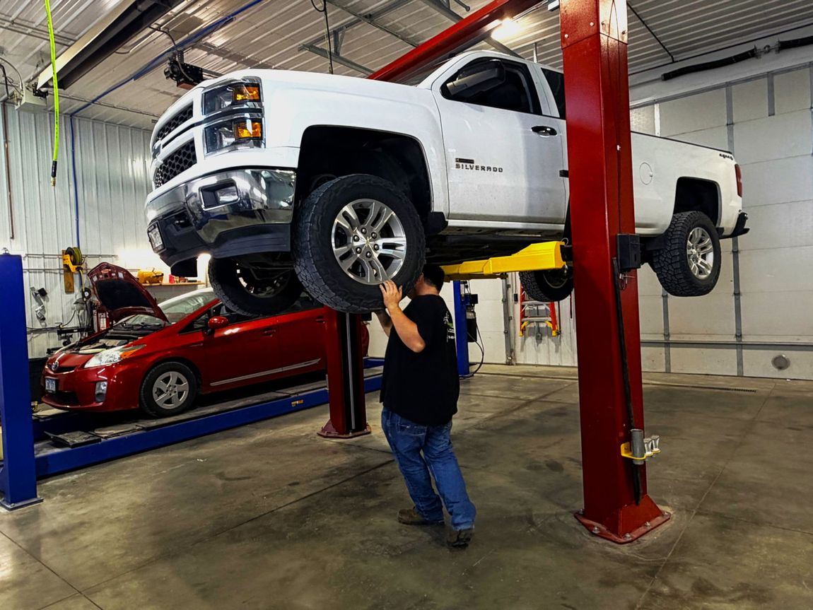 Mechanic working under a car, illuminated by a work light, wearing a blue jumpsuit.