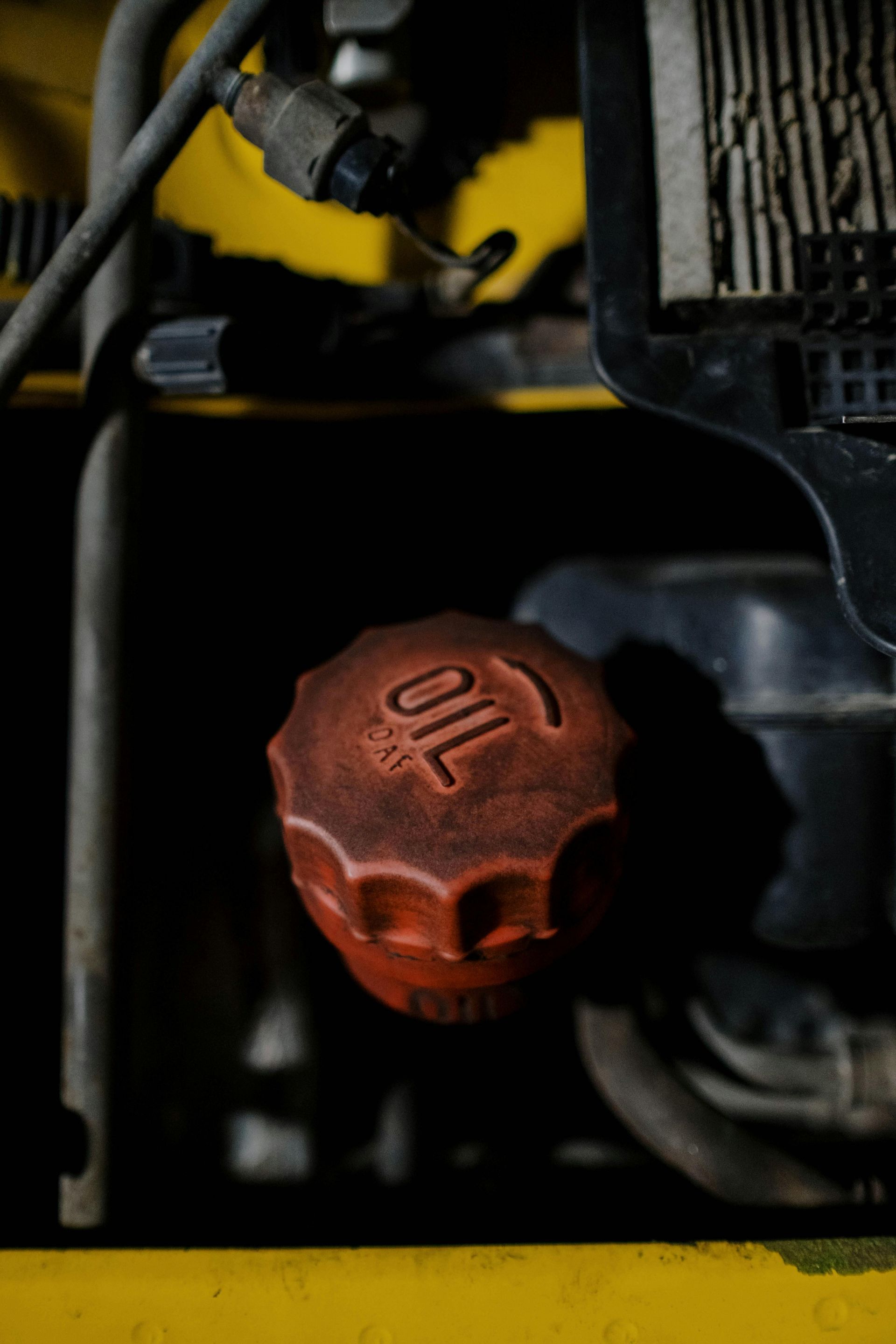 Red oil cap on a yellow machine, with "OIL" embossed. Dark setting.