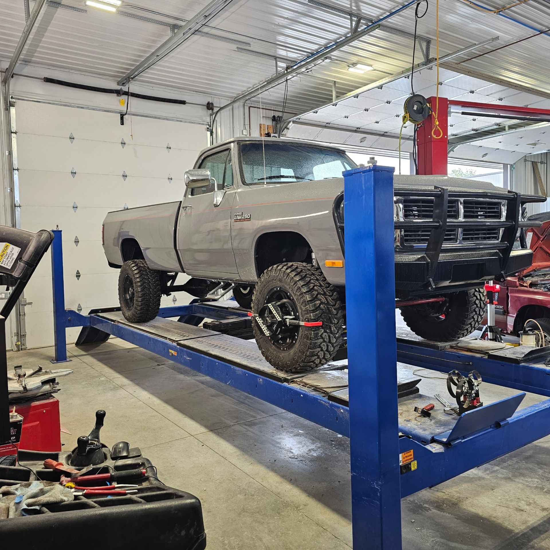 Gray pickup truck on a blue lift inside a garage. The truck has large tires and a black bull bar.