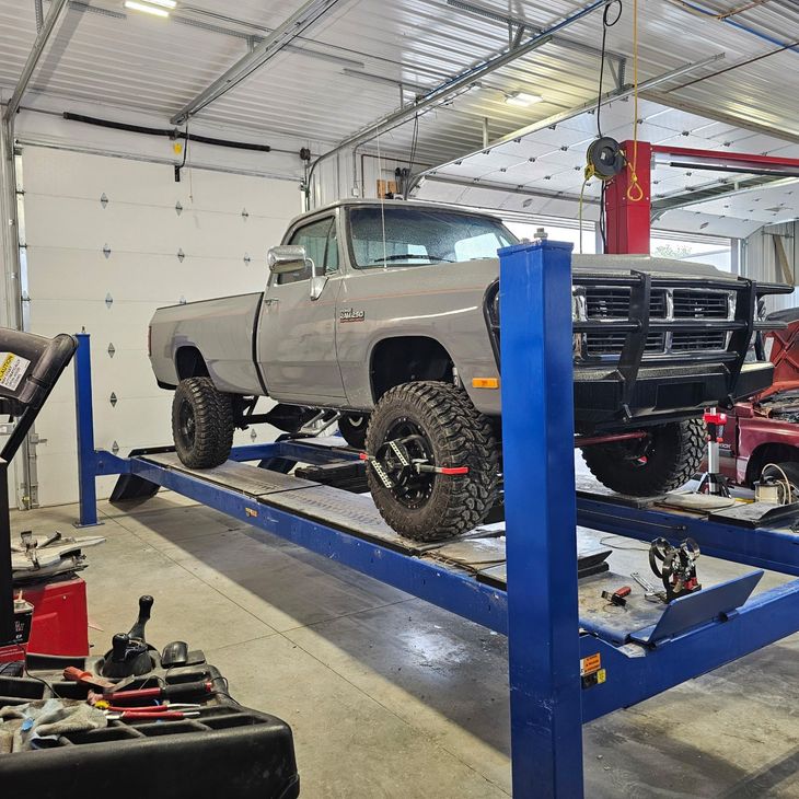 Gray pickup truck on a blue lift inside a garage. The truck has large tires and a black bull bar.