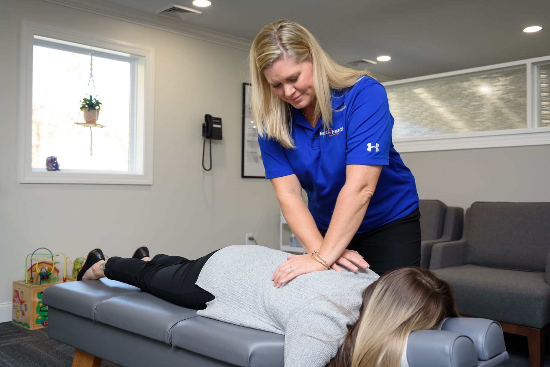A woman in a blue shirt is giving a woman a massage on a table.