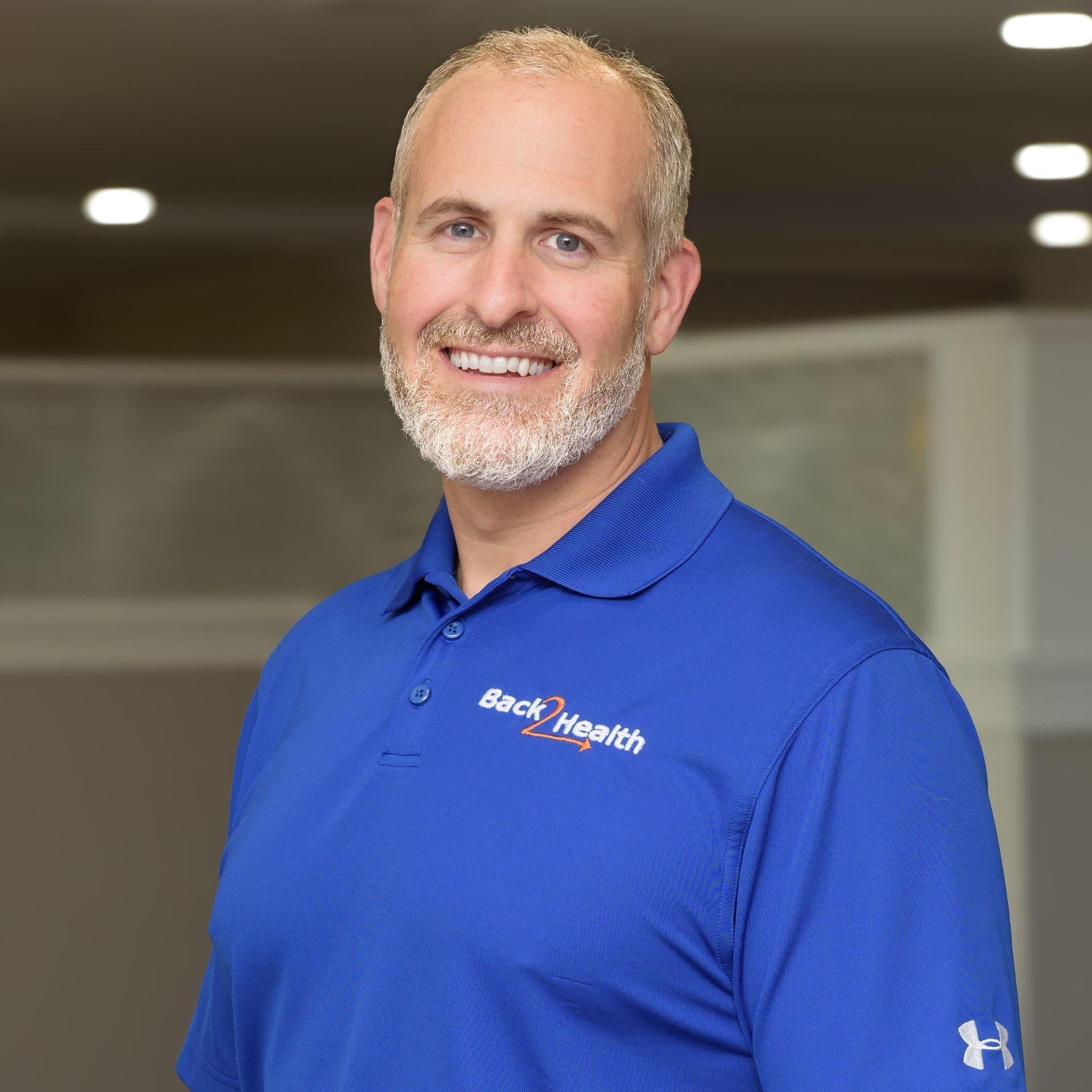 A man with a beard is wearing a blue polo shirt and smiling.
