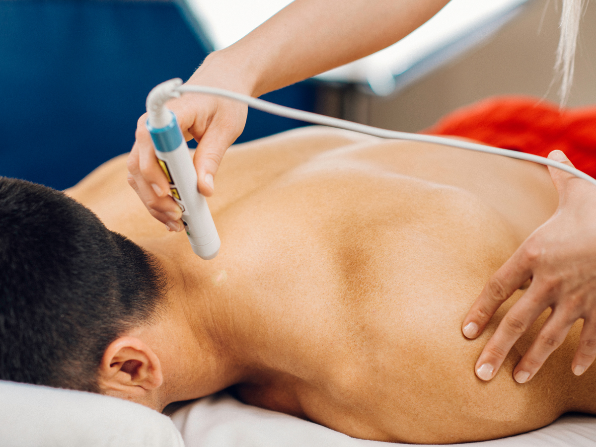 A woman is sitting at a desk with a computer and holding her back in pain.