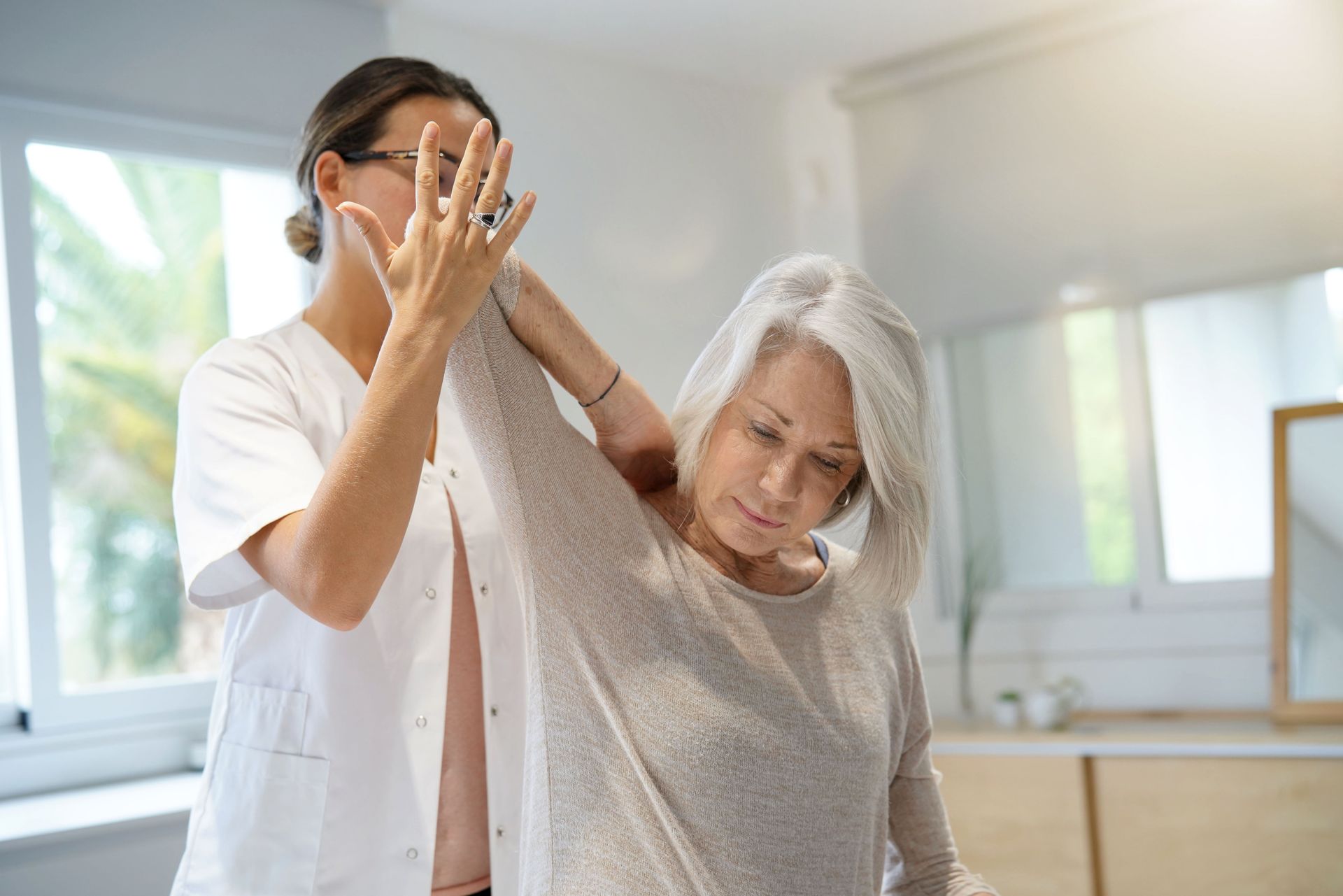 Therapist stretches patient's arm; sunny room. Therapist stretches patient's arm; sunny room.