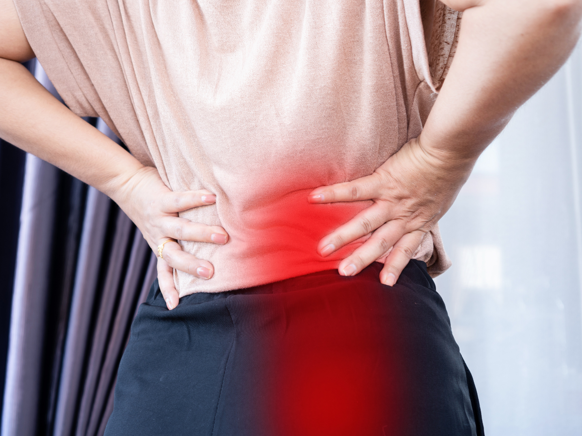 Woman holding lower back in pain, red highlight indicates injury.